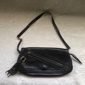 May include: A black leather shoulder bag with a gold zipper and a gold tassel. The bag has a flap closure and a small gold logo on the front.