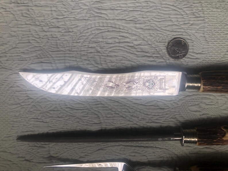 May include: A knife with a decorative blade featuring an etched design and a brown handle. The blade has a silver finish. A quarter is next to the knife for scale. The knife is part of a set.