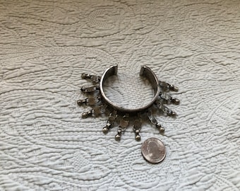 May include: A silver bracelet with a decorative design of dangling charms. The bracelet is open and has a circular shape. A US quarter is included for size reference.