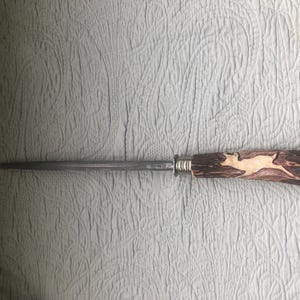 May include: A steel knife sharpener with a decorative handle. The handle is made of brown wood and features a carved image of a deer. The handle is approximately 5 inches long.
