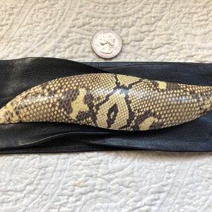 May include: A black leather belt with a snakeskin buckle. The buckle is a light brown color with a dark brown pattern.