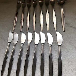 May include: A set of 12 silver-toned flatware pieces, including forks and butter knives. The flatware is arranged in two rows on a white surface.