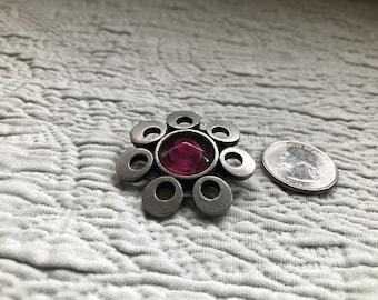 May include: A silver brooch with a pink glass center surrounded by eight silver circles.