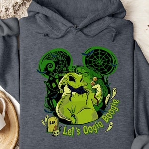 May include: Dark gray hooded sweatshirt featuring a green Oogie Boogie design with a haunted house, bats, and spiderwebs. The text "Let's Oogie Boogie" is printed in green. The design is in the shape of Mickey Mouse ears.