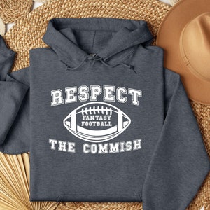 May include: A dark gray hooded sweatshirt with the text "RESPECT THE COMMISH" and a white football graphic with the text "FANTASY FOOTBALL" inside.
