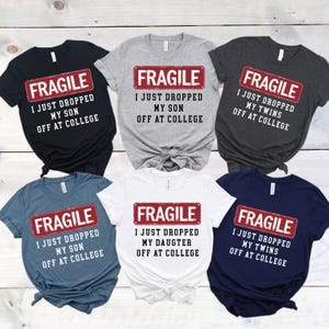 May include: Six t-shirts in various colors, each featuring the word "FRAGILE" above the text "I JUST DROPPED MY [SON, DAUGHTER, or TWINS] OFF AT COLLEGE" in a red and white design. The shirts are black, gray, dark gray, blue, white, and navy.