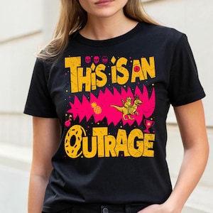 May include: Black t-shirt with a distressed yellow and pink graphic. The graphic reads "This is an Outrage" with a cartoon dinosaur and rider, skulls, a pineapple, a donut, and a trophy.