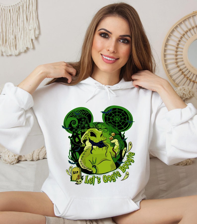 May include: White hoodie featuring a green Oogie Boogie design with a haunted house, bats, and spiderwebs. The design includes the text "Let's Oogie Boogie" and ghost illustrations. A tombstone with "RIP" is also visible.