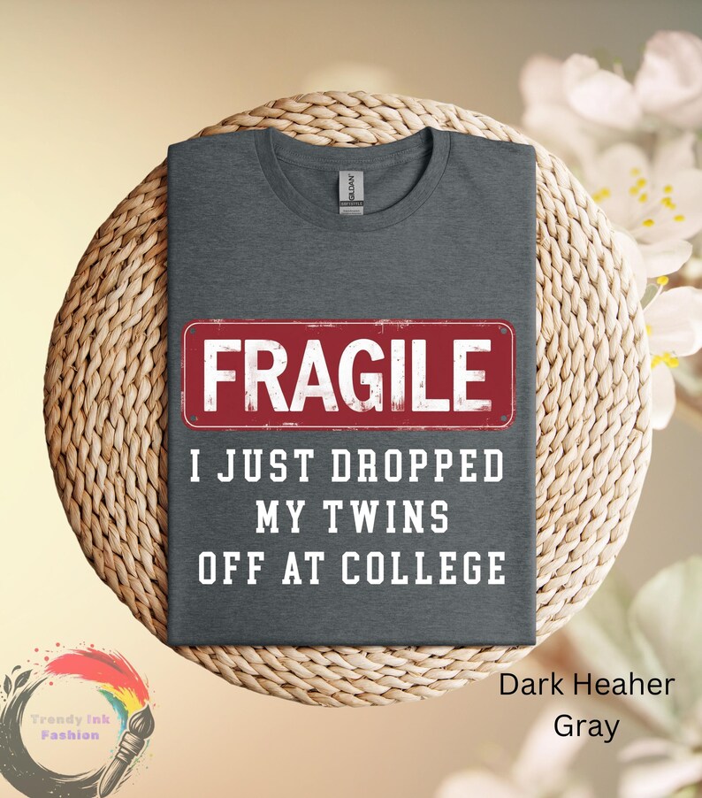May include: Dark heather gray t-shirt with the word "FRAGILE" in a red rectangle, and the text "I JUST DROPPED MY TWINS OFF AT COLLEGE" in white. The shirt is displayed on a woven surface.