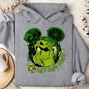 May include: A gray hooded sweatshirt featuring a green Oogie Boogie design with a haunted house and bats. The text "Let's Oogie Boogie" is printed in green. The design is reminiscent of a popular Halloween movie.