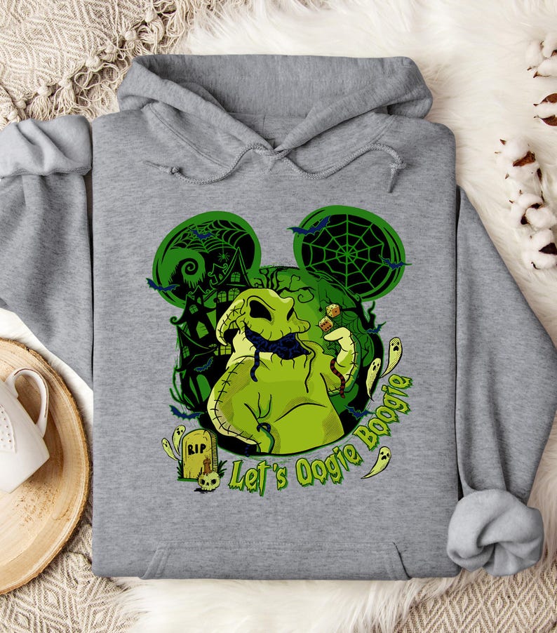 May include: A gray hooded sweatshirt featuring a green Oogie Boogie design with a haunted house and bats. The text "Let's Oogie Boogie" is printed in green. The design is reminiscent of a popular Halloween movie.