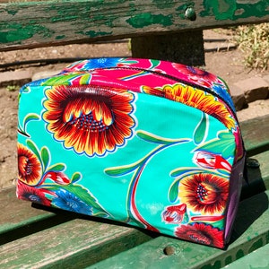 May include: A turquoise blue makeup bag with a floral print featuring red, yellow, and orange flowers. The bag has a black zipper and a purple lining.
