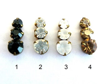 May include: Four sets of three rhinestones in different colors: black, clear, white, and amber. Each set is attached to a metal base.