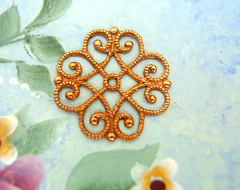 May include: A gold-colored metal charm with a decorative, intricate design. The charm features a repeating pattern of swirls and loops, creating a delicate and ornate look.
