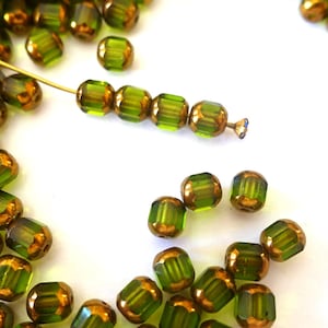 May include: A collection of olive green and gold-toned glass beads. The beads are faceted and cylindrical, with a metallic gold finish on the ends. Some beads are strung on a gold wire, suggesting their use in jewelry making or crafts.