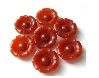 May include: Seven orange flower-shaped buttons with a raised center. The buttons are made of a smooth, glossy material.