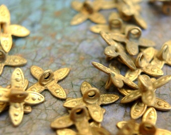May include: A group of gold-toned metal flower-shaped buttons with a loop on the back. The buttons are scattered on a textured, light blue surface.
