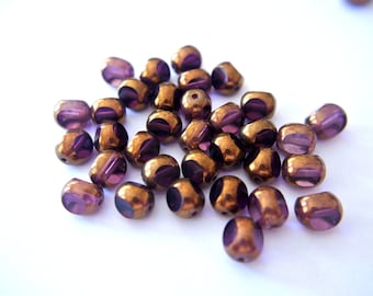 May include: A group of small, round, purple glass beads with a metallic gold finish.