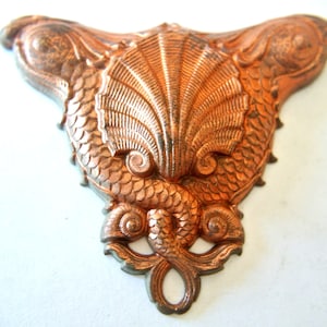 May include: A copper-colored metal ornament shaped like two fish flanking a seashell. The ornament has a detailed design with scales and a textured surface.
