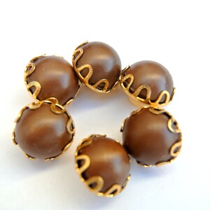 May include: Six brown buttons with gold trim. The buttons are round and have a smooth surface.