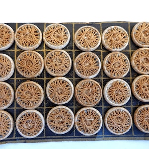 May include: A card of 25 brown and white woven buttons. The buttons are arranged in a grid pattern on a black and gold card.