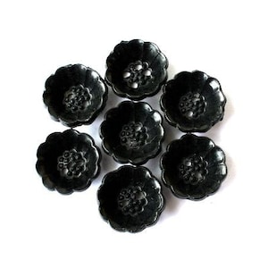 May include: Seven black plastic buttons with a floral design. The buttons are arranged in a circle.