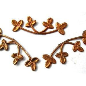 Può includere: Due rametti di foglie in metallo dorato con un design delicato e intricato. Ogni rametto ha cinque foglie e uno stelo curvo.