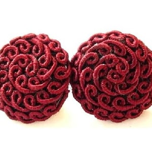 May include: A pair of red, round, fabric earrings with a swirling, textured design.