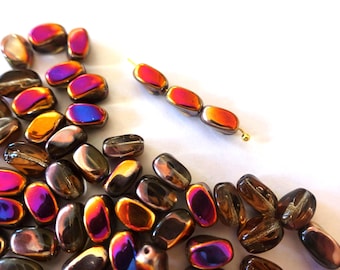Può includere: Un assortimento di perline ovali iridescenti nei toni del marrone, viola, arancione e oro. Alcune perline sono infilate su un filo dorato. Le perline sono sparse su una superficie bianca, ideali per la creazione di gioielli. Misurano circa 1 cm.