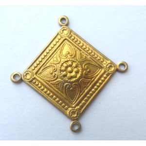 Puede incluir: Pendiente de metal dorado con forma cuadrada y un intrincado diseño floral. El pendiente tiene cuatro bucles para sujetarlo a una cadena u otras joyas.