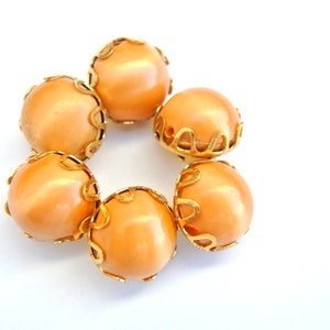 May include: Six peach-colored buttons with gold metal trim. The buttons are arranged in a circle.