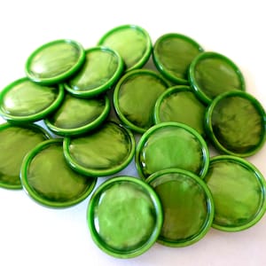 May include: A pile of glossy, round, green glass beads with a slightly textured surface. The beads are a vibrant shade of green and have a raised, circular border. They are scattered on a white background.