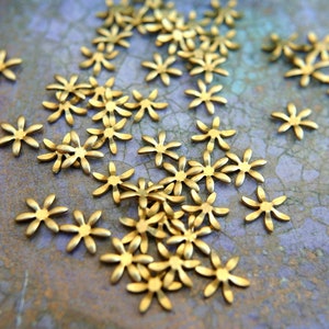 Può includere: Una spolverata di decorazioni metalliche a forma di fiore dorate su uno sfondo viola testurizzato.