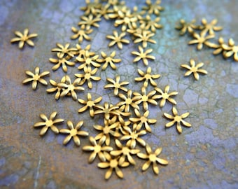 May include: A scattering of gold-toned metal flower-shaped embellishments on a textured purple background.