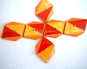 May include: A collection of six geometric buttons in shades of orange and yellow, each with a diagonal red accent. The buttons have two small black holes for sewing. The buttons are arranged in a star-like pattern.