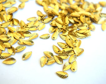 May include: A large quantity of gold-colored metal leaf-shaped embellishments. The leaves have a textured surface and a small hole at the top.