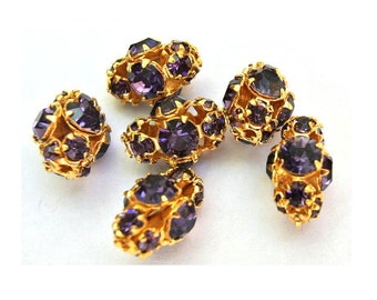 May include: Six gold-toned, clustered beads with faceted, deep purple gemstones. The beads are arranged on a white surface, showcasing their intricate design and sparkling appearance. These beads are suitable for jewelry making.