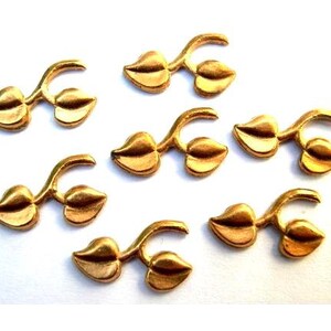 May include: Eight gold-coloured metal leaf embellishments, each featuring two leaves connected by a stem. These decorative accents are perfect for adding a touch of nature to crafts and projects.