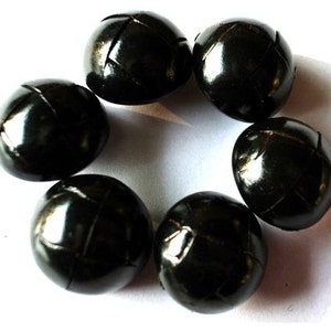 May include: A collection of seven glossy, black buttons arranged in a circular pattern. Each button has a rounded shape with a textured, cross-stitched design. The buttons are set against a white background.
