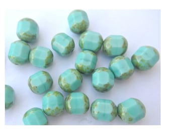 Può includere: Una collezione di perline di vetro blu turchese con una finitura macchiettata di verde e oro. Le perline sono sfaccettate e hanno una forma leggermente irregolare.