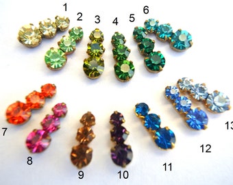 May include: Thirteen sets of three rhinestones in various colors, including green, blue, orange, pink, and purple. Each set is arranged in a staggered pattern on a white background.