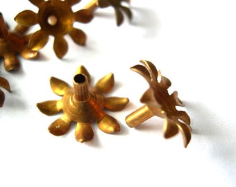 May include: A set of six gold-toned metal candle holders shaped like flowers with eight petals. Each holder has a small hole in the center for a candle wick.