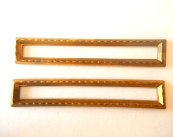 May include: Two gold-colored metal rectangular frames with a decorative border. The frames are empty and ready to be filled with a name or other text.
