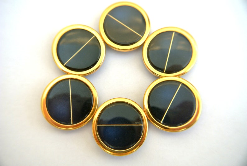 May include: Seven round, gold-rimmed buttons with black centers and a thin gold line across the center.