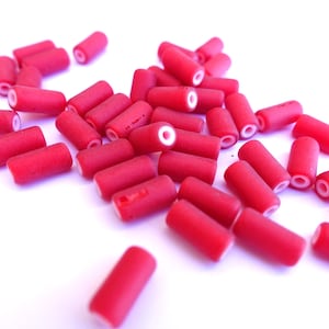 May include: A collection of small, cylindrical red beads with white centers scattered on a white surface. The beads are evenly sized and appear to be made of a solid material. The image is well-lit, highlighting the texture and color of the beads.