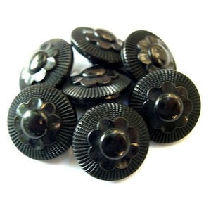 May include: A group of seven black plastic buttons with a raised flower design. The buttons are round and have a shiny finish.