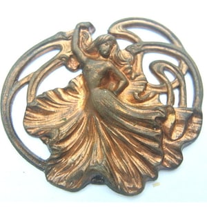Può includere: Una spilla vintage in metallo color rame con una donna stilizzata in un abito fluido. Il design ricorda lo stile Art Nouveau.