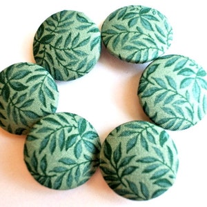 May include: Six green fabric buttons with a leafy pattern. The buttons are arranged in a circle.