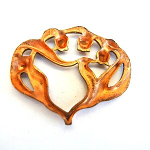 Pu&ograve; includere: Un ciondolo in metallo color rame a forma di cuore stilizzato con dettagli floreali. Il ciondolo ha un design a taglio, rivelando lo spazio aperto all'interno della forma del cuore.
