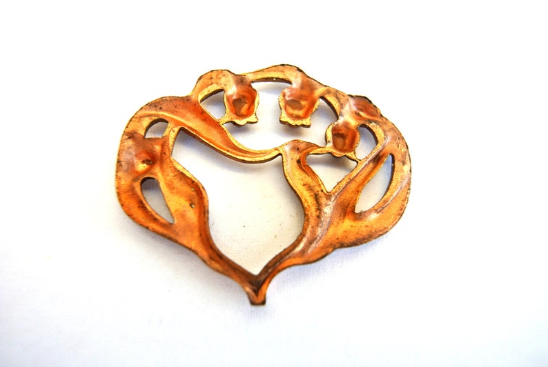 Pu&ograve; includere: Un ciondolo in metallo color rame a forma di cuore stilizzato con dettagli floreali. Il ciondolo ha un design a taglio, rivelando lo spazio aperto all'interno della forma del cuore.